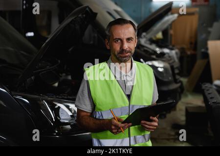 Waist up portrait of mature male worker looking at camera while inspecting vehicles at car factory quality control Stock Photo