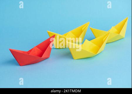 red paper boat leads a group of yellow paper boats Stock Photo