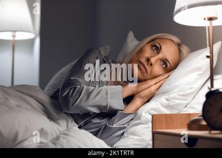 Stressed mature woman lying in bed at night Stock Photo