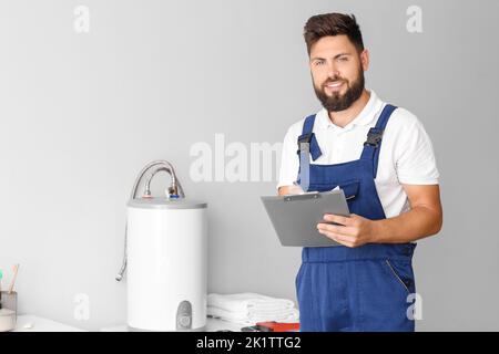 Male plumber writing on clipboard near boiler in bathroom Stock Photo