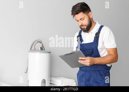 Male plumber writing on clipboard near boiler in bathroom Stock Photo