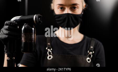 The master of instant tanning holds a spray pen with lotion. Express tan in a beauty salon. Stock Photo