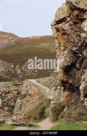 A vertical closeup of rocky cliffs and hills in valley next to country trail in the countryside Stock Photo