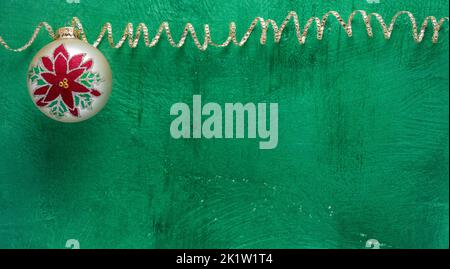 Christmas or winter holiday theme with ball ornament and sparkle ribbon on bright green textured background Stock Photo