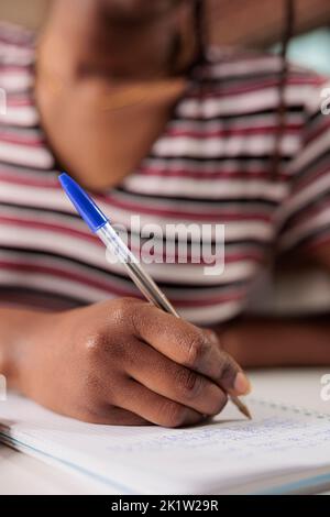 African american woman hand writing with pen in notepad at desk closeup. Student taking notes in planner close view, studying, preparing for exam, doing homework in notebook Stock Photo