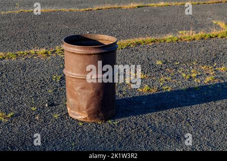 Garbage can in a metal barrel outside on asphalt at the parking lot. Stock Photo