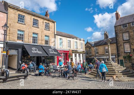 People sat and relaxing outside the Pig in Muck cafe and restaurant in afternoon sunlight in the Northumberland market town of Alnwick on market day. Stock Photo
