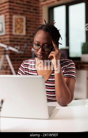 Tired woman having migraine, thoughtful employee working on laptop, suffering from headache symptom. Exhausted remote worker feeling unwell, busy stressed overworked freelancer Stock Photo