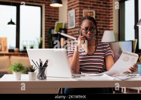 Freelancer talking on smartphone, discussing report, remote analyst looking at charts and diagrams. Employee working from home, answering mobile phone call, chatting about research Stock Photo