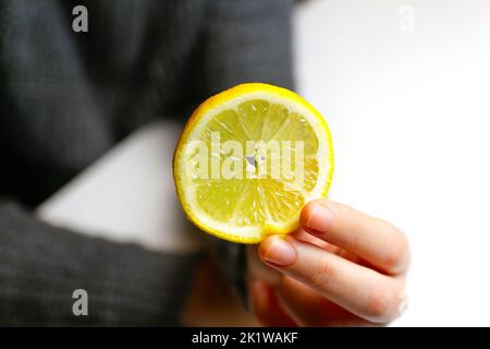 Defocus female hand holding one yellow slice lemon fruit. Hand holds lemon slice on white background. Closeup. Out of focus. Stock Photo