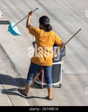 SAMUT PRAKAN, THAILAND, MAY 26 2022, A young woman with a broom and a shovel cleans the street Stock Photo