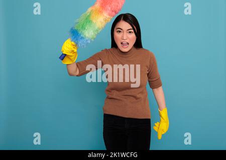 Asian angry energetic and confidence houseworker from work holding colorful dust brush in yellow gloves, Cleaning home concept, Housewife feeling frustrated and negative from daily chores Stock Photo