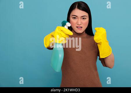 Angry frustrated asian young housewife in rubber gloves and detergent spray standing in a fight pose, Cleaning home concept, Aggressive energetic housekeeper feeling negative Stock Photo