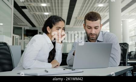 Woman professional manager consultant saleswoman shows man client availability goods on laptop helps to place order in online store colleagues working Stock Photo