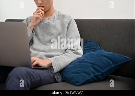 A professional Asian male programmer or freelancer working from home, using laptop computer to manage his tasks. cropped shot Stock Photo