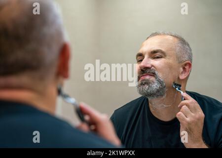 Middle-aged handsome man using razor in bathroom Stock Photo