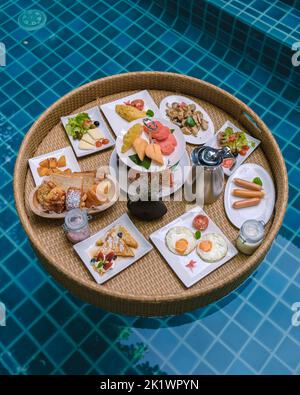 Top view of floating breakfast in the swimming pool, floating breakfast in the pool with bread eggs and fruit, and coffee Stock Photo