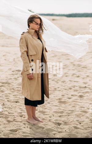 Female loneliness. Fall nostalgia. Despair sorrow. Art portrait of thoughtful depressed woman in beige trench coat with flying away hair in cold wind Stock Photo