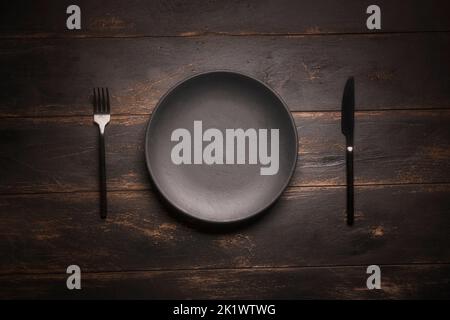 An empty black plate and cutlery on a wooden table top view Stock Photo