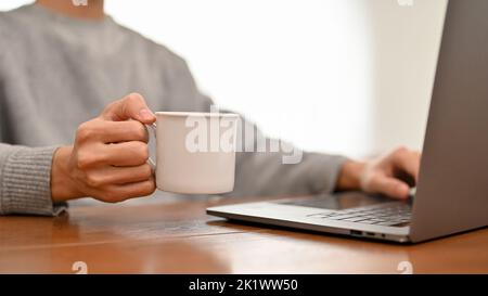 A businessman or male college student working on his project, researching information on the internet, using laptop computer while having coffee. crop Stock Photo