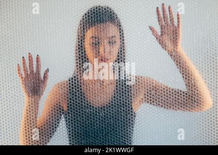Woman protection. Defocused portrait. Self isolation. Female discrimination. Hopeless lady in black top trapped behind transparent bubble wrap texture Stock Photo
