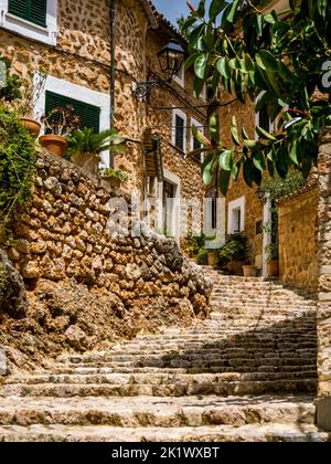 Narrow uphill alley named Carrer Església with curved cobbled steps in the idyllic mediterranean mountain village Fornalutx lined with mediterranean s