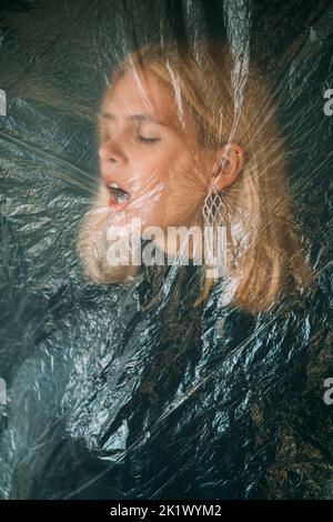 Female abuse. Defocused art portrait. Domestic violence. Disturbed hurt blonde woman face with closed eyes isolated behind wrinkled texture transparen Stock Photo
