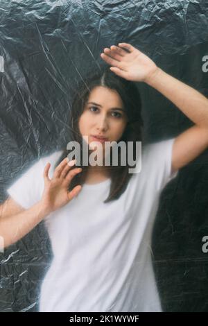 Female loneliness. Defocused portrait. Misery tragedy. Regret sorrow. Desperate sad woman trapped behind wrinkled texture transparent polyethylene fil Stock Photo