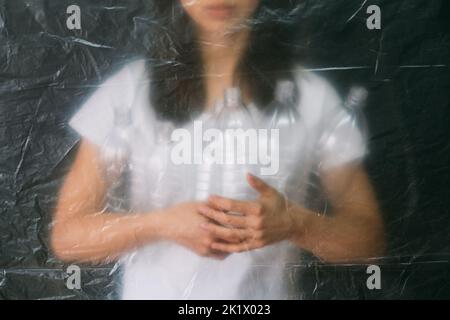 Plastic recycling. Defocused silhouette. Waste management. Ecology problem. Female volunteer holding empty bottles behind wrinkled texture polyethylen Stock Photo