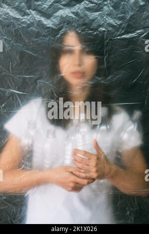 Plastic pollution. Defocused silhouette. Garbage collection. Zero waste. Volunteer woman holding used bottles behind wrinkled texture polyethylene fil Stock Photo