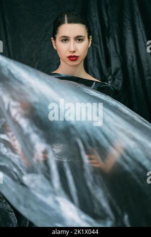 Beauty portrait. Plastic surgery. Aesthetic cosmetology. Confident woman with perfect face skin night makeup red lips posing in wrinkled transparent p Stock Photo