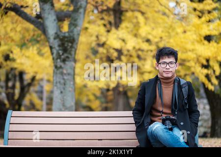 Happy man enjoy at the park outdoor in Autumn season, Asian traveler in coat and camera against Yellow Ginkgo Leaves background Stock Photo