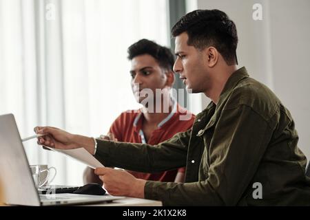 Software developer pointing at computer screen when sharing his idea with colleague Stock Photo