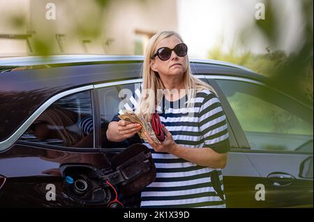 worried woman with euro cash at the car, put money to car tank, the concept of rising fuel prices Stock Photo