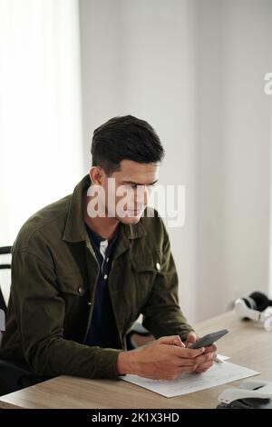 Serious software developer checking text messages on smartphone instead of working on project Stock Photo