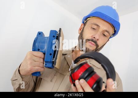 builder considering wearing earmuffs while using sander Stock Photo