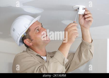 male builder screwing fixture to ceiling Stock Photo