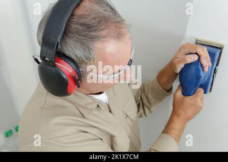 builder in hardhat sanding wall indoors Stock Photo