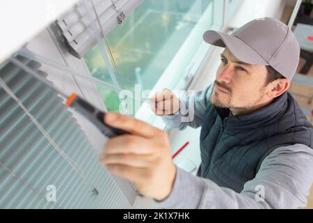 construction worker man install blinds on plastic white upvc windows Stock Photo