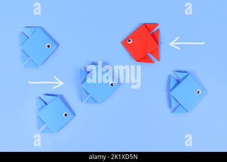 Red paper fish swimming swimming against the current in opposite direction of blue fish Stock Photo