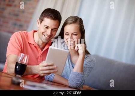 Taking a trip down memory lane. A young couple using a digital tablet at home. Stock Photo