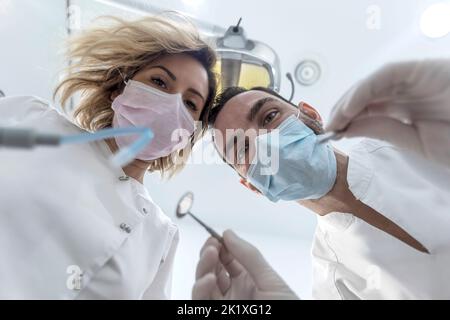 Man and woman two dentists in medical face masks and rubber gloves doing treatment, low angle shot from dental chair. Stock Photo
