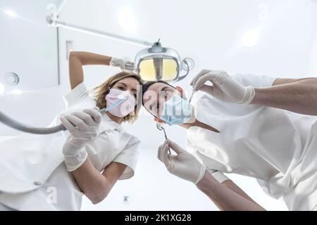 Man and woman two dentists in medical face masks and rubber gloves doing treatment, low angle shot from dental chair. Stock Photo