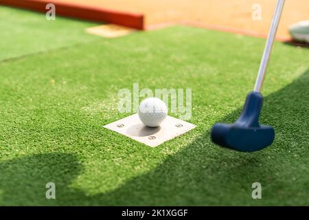A club prepares to hit a ball during a mini golf game Stock Photo