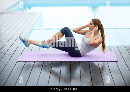 Perfect abs take work. a gorgeous young woman doing yoga outdoors beside a pool. Stock Photo