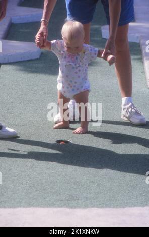 A vertical shot of a parent holding a toddler while croquet ball falls in the hole Stock Photo