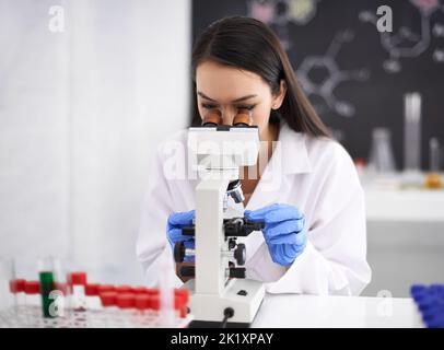 Taking a closer look at the sample. Profile of a female scientist viewing a sample through a microscope. Stock Photo