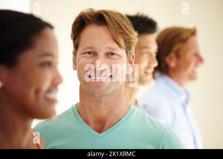 He knows that with diversity the future is secure. Diverse group of smiling adults standing in a row with one man looking at the camera. Stock Photo
