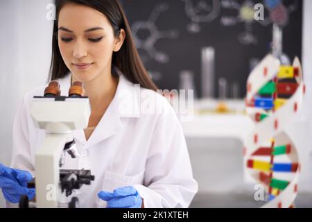 Unlocking the secrets of genetics. Profile of a female scientist viewing a sample through a microscope. Stock Photo