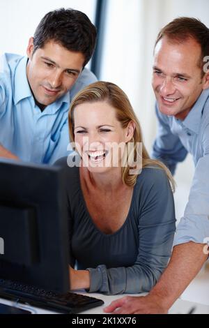 In this office laughter is the only medicine. three happy co-workers laughing while watching a PC screen. Stock Photo